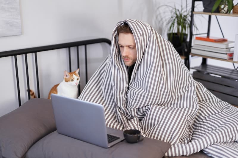 Ein Mann sitzt mit Decke vor dem Laptop, wie funktioniert die Krankmeldung per Mail?