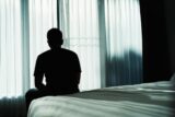 Ein Mann sitzt alleine auf dem Bett, welche Folgen hat soziale Isolation?